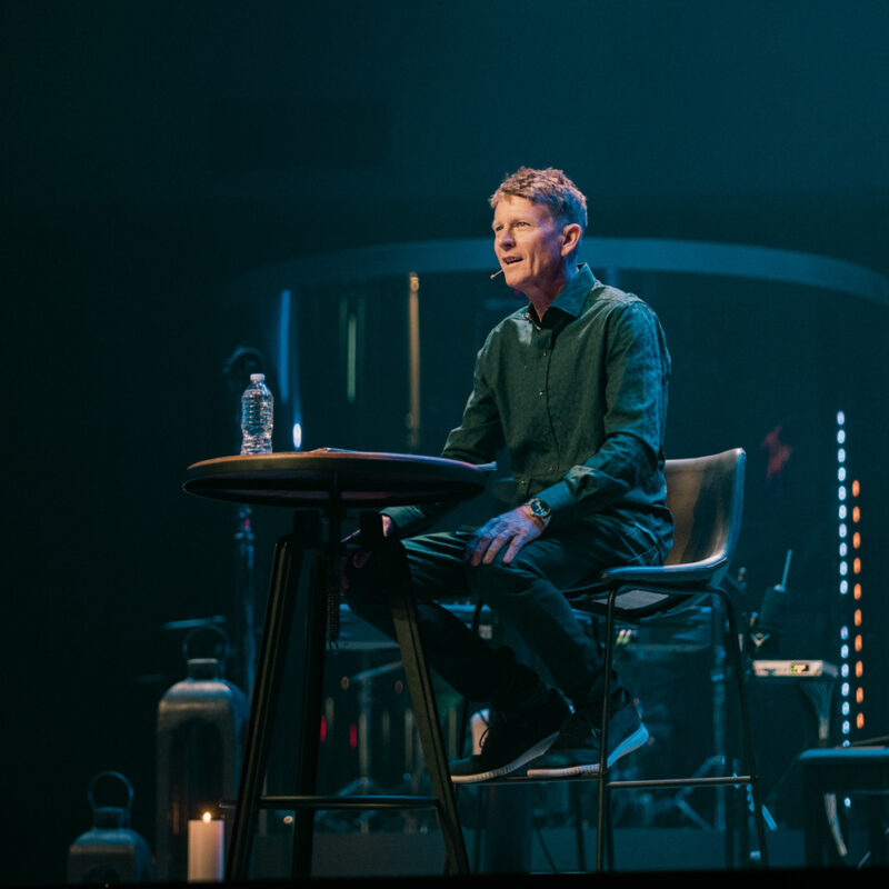 Pastor seated on stage delivering a message at Coastline Community Church with atmospheric stage lighting in Indian Harbour Beach Florida